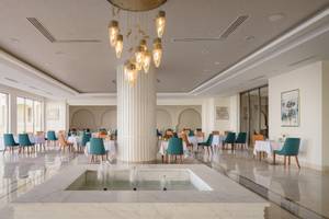 Innenbereich des Xanadu Makadi Bay Hotels mit modernem Restaurant, Wasserbrunnen und vielen Tischen und Stühlen.