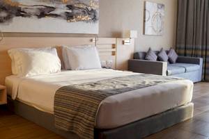 Hotelzimmer im Xanadu Makadi Bay mit zwei Betten, Kissen, einem Tisch, einer Couch und Kunstwerken an der Wand.
