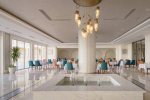 Innenbereich des Xanadu Makadi Bay Hotels mit modernem Design, großen Tischen und Stühlen, einer zentralen Säule und einem Wasserbrunnen.