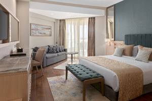 Innenansicht eines Hotelzimmers im Xanadu Makadi Bay mit einem großen Bett, einem Sofa, einem Fernseher und einem Schreibtisch.