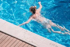Frau schwimmt im blauen Pool des Aimia Hotels