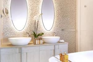 Badezimmer im Ikos Dassia Hotel mit zwei Waschbecken und Spiegeln.