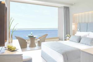 Zimmer mit Meerblick im Ikos Dassia Hotel mit Bett, Tisch und Stühlen.