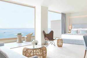 Modernes Hotelzimmer mit Meerblick im Ikos Dassia, mit großen Fenstern, einem Bett, und einem Ausblick auf den Ozean.