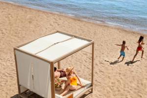 Familie genießt den Strandbereich im Ikos Dassia Hotel, mit Sonnenliege und spielenden Kindern.