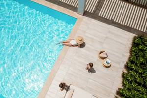 Luftaufnahme eines Pools mit Gästen im Hotel Ikos Dassia, einer Frau schwimmt und zwei Kinder sitzen neben dem Pool.