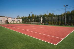 Tennisplatz im Ikos Dassia Hotel mit rotem Boden und grünem Rasen.