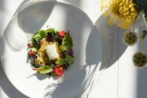 Ein Salat mit Fisch auf einem weißen Teller, umgeben von bunten Blüten auf einem Tisch.