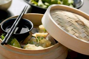 Dampfende asiatische Dumplings in einem Korb mit Soße und Chopsticks