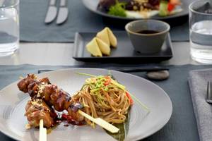 Ein Teller mit asiatischem Gericht im Hotel Ikos Odisia, bestehend aus gegrilltem Fleisch und Nudeln.