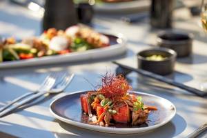 Speisen auf dem Tisch im Hotel Ikos Odisia, einschließlich eines Tellers mit Fleisch und Gemüse und einem Glas Wein.