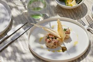 Ein weißer Teller mit zwei gebratenen Fleischgerichten und Beilagen, serviert im Ikos Olivia Hotel.