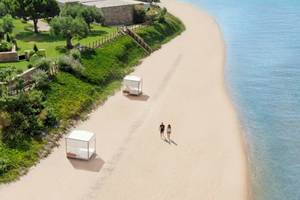Zwei Personen, die auf einem Strand entlanggehen, mit zwei weißen Bettzelten auf der Seite.