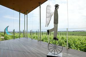 Statue eines Mannes auf Einrad auf Terrasse vor Weinberg bei Ikos Olivia Hotel