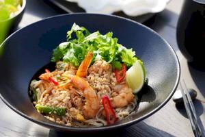 Ein Teller mit Shrimp-Nudel-Gericht in einer schwarzen Schüssel, garniert mit Limettenscheibe und Gemüse.