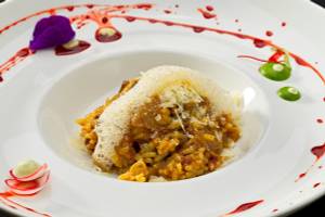 Ein Gericht in einem weißen Teller mit roter Sauce und grünen Beilagen.