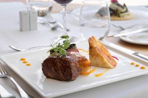 Ein Essen am Tisch des H10 Blue Mar Boutique Hotels mit Steak, Beilagen und Getränken.