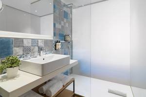 Badezimmer im H10 Casa del Mar Hotel mit blauen und grauen Fliesen, weißem Waschbecken und Glasdusche.