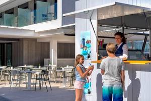 Zwei Kinder kaufen Eis von einer Verkäuferin in einem weißen Eiswagen vor dem H10 Casa del Mar Hotel.