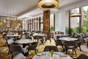 Innenansicht des Restaurants im Atlantis The Royal Hotel mit eleganten Tischen, Stühlen und goldenen Kronleuchtern.