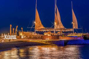 Nachtansicht des Rixos Premium Magawish Suites & Villas mit beleuchteten Segeln und Loungebereich am Wasser.