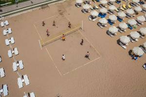 Besuch des Melas Resorts, Leute spielen Volleyball am Strand vor vielen Sonnenliegen
