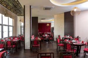 Innenansicht des Restaurants im Melas Resort mit roten Stühlen und Tischen, dekorativ beleuchtet.