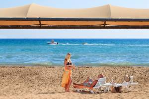 Strandszene mit Novum Garden Side Hotel, Frau in Bikini und Mann auf Sonnenliegen