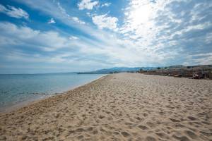 Eine breite Sandstrand mit Sonnenliegen und Sonnenschirmen unter einem bewölkten Himmel.