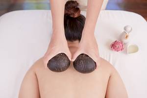 Massage-Behandlung im Bandara Resort & Spa, Samui, mit Kokosnuss-Massagewerkzeugen auf dem Rücken einer Frau.