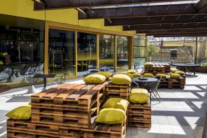 Terrasse des Novotel London Canary Wharf mit gelben Kissen und Holzpalettenmöbeln.