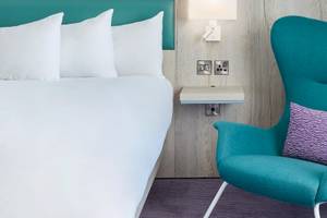 Ein modernes Hotelzimmer mit einem weißen Bett und einem blauen Sessel im Leonardo Hotel London Croydon.