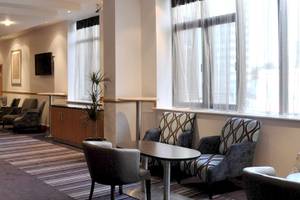 Leonardo Hotel London Croydon Lobby mit Tischen, Stühlen und Pflanzen.