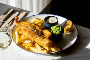 Fisch und Chips Gericht auf Teller mit Pommes und Saucen.