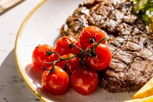 Gegrilltes Steak mit Tomaten und Pommes auf einem weißen Teller.