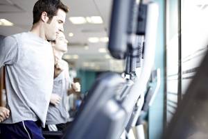 Ein Mann läuft auf einem Laufband im Fitnessstudio, während ein anderer Mann im Hintergrund läuft.
