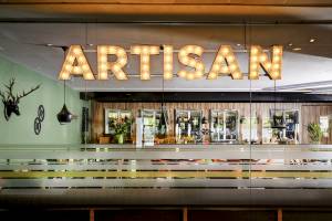 Innenansicht der Artisan Bar im Novotel London West mit großem Leuchtschriftzug und Holzelementen.