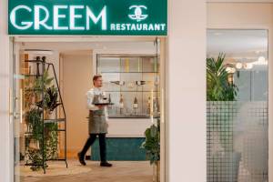Eingang des Greem Restaurants im Novotel Paris Tour Eiffel mit Kellner, der Flaschen und Weingläser präsentiert.