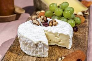 Eine Schnitte von weißem Käse mit Nüssen und Obst auf einem Holzbrett.