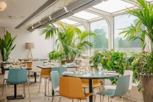 Innenansicht des Restaurants im Novotel Paris Tour Eiffel mit runden Tischen, farbenfrohen Stühlen und großen Fenstern.