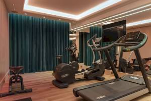 Fitnessraum im Victor Hugo Paris Kléber Hotel mit Laufband, Rudergerät und blauen Vorhängen.