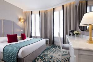 Ein elegantes Hotelzimmer im Victor Hugo Paris Kléber mit Bett, Schreibtisch und Fenstern.