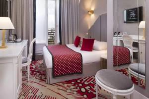 Hotelzimmer im Victor Hugo Paris Kléber mit einem Bett, roten Kissen und einem Schreibtisch.