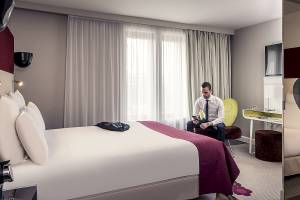 Mann sitzt auf Stuhl neben Bett im Zimmer des Mercure Paris Bercy Bibliothèque Hotels