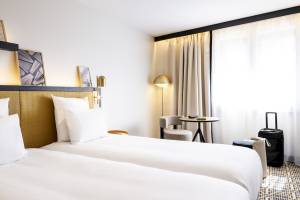 Doppelzimmer im Mercure Paris Bercy Bibliothèque mit zwei Betten, Nachttischen und einem Reisekoffer.