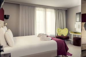Schlafzimmer im Mercure Paris Bercy Bibliothèque Hotel mit Bett, Kissen, Bademänteln und Möbeln.