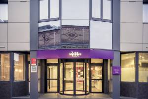 Foto des Mercure Paris Bercy Bibliothèque Hotels, zeigt den Eingang mit einer Glasdrehtür und einer violetten Überdachung.