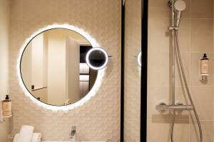 Badezimmer des Mercure Paris Bercy Bibliothèque mit beleuchtetem Spiegel und Duschvorrichtung.