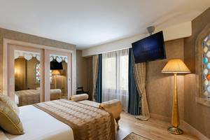 Hotelzimmer im Titanic Mardan Palace mit Doppelbett, Fernseher, Lampe und Spiegeln.