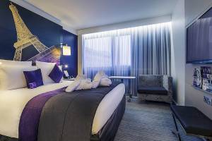 Hotelzimmer im Mercure Paris Centre Tour Eiffel mit Eiffelturm-Wandbild, Bett, Sessel und Fernseher.